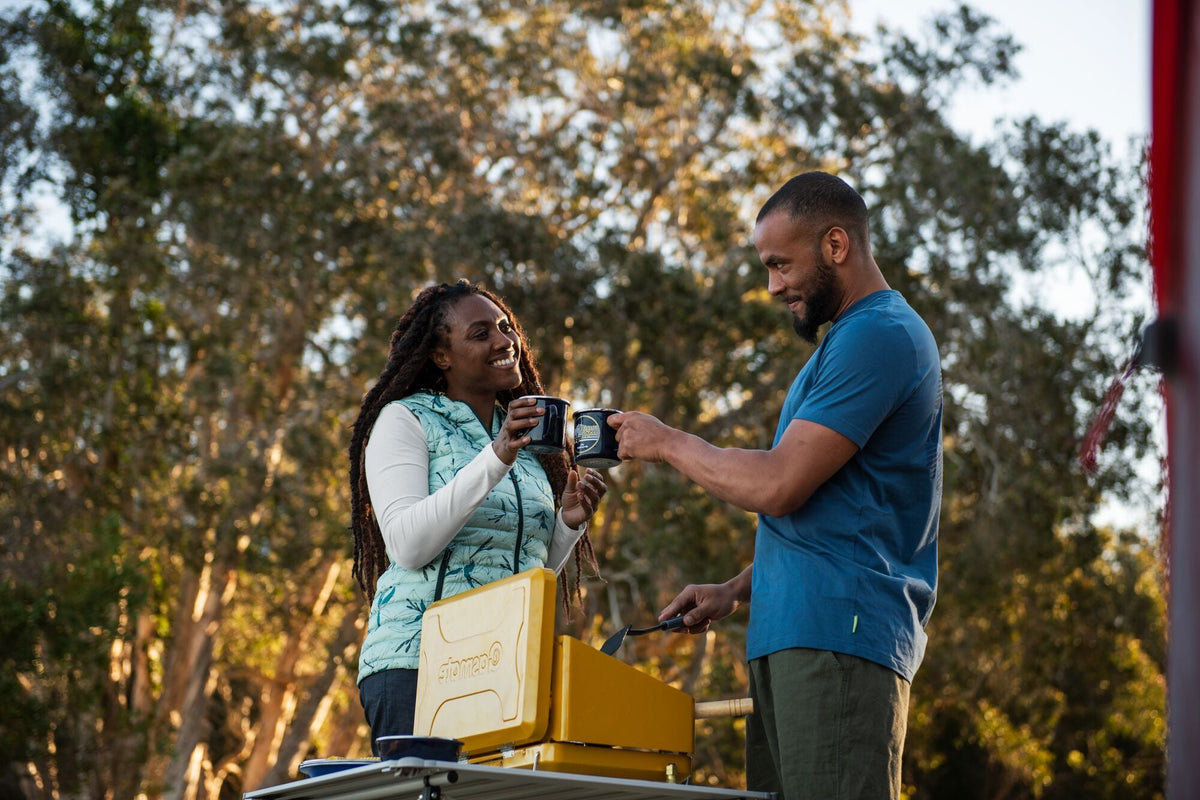 A couple is preparing a meal on a camping stove